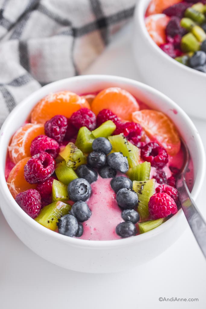 rainbow smoothie bowl with a spoon on a white table with kitchen towel in background.