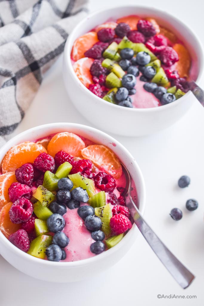 rainbow fruit smoothie bowl in two white bowls with spoons on a white table. 