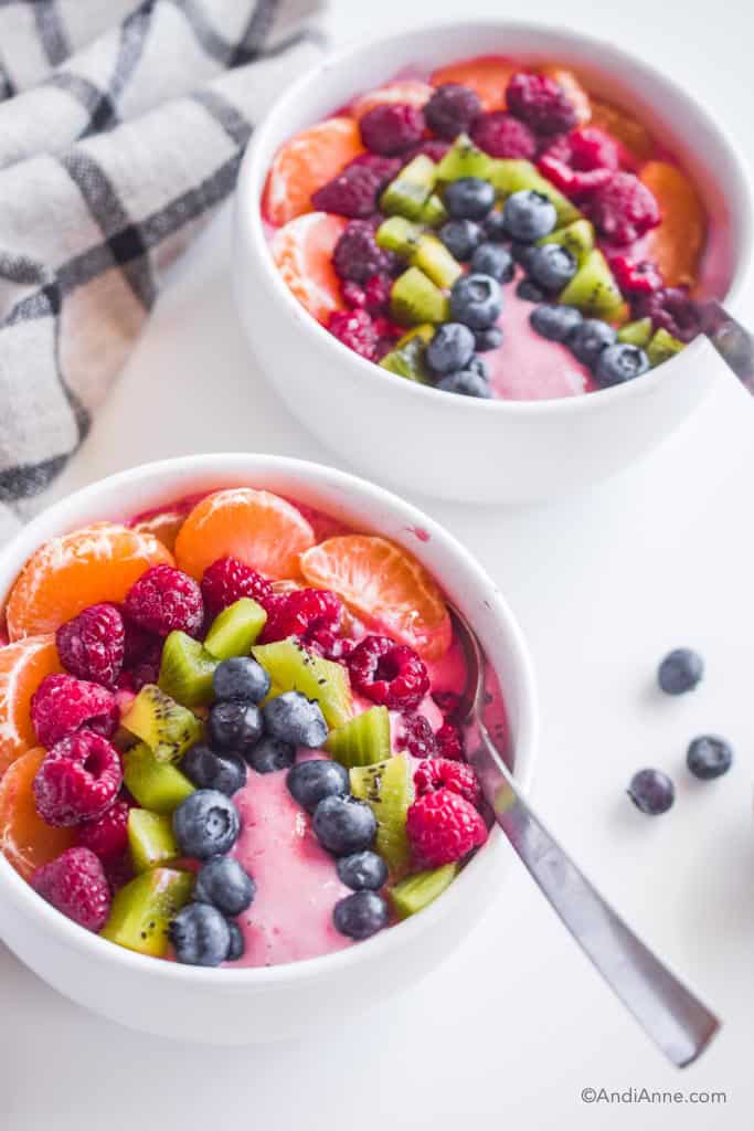 rainbow fruit smoothie bowl in two white bowls with spoons on a white table.