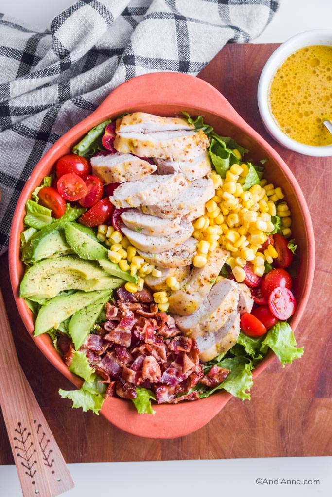 maple dijon chicken avocado salad in a terra cotta bowl with dressing in white bowl beside it.
