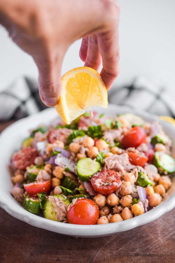 hand squeezing lemon overtop of chickpea tuna salad in a white bowl