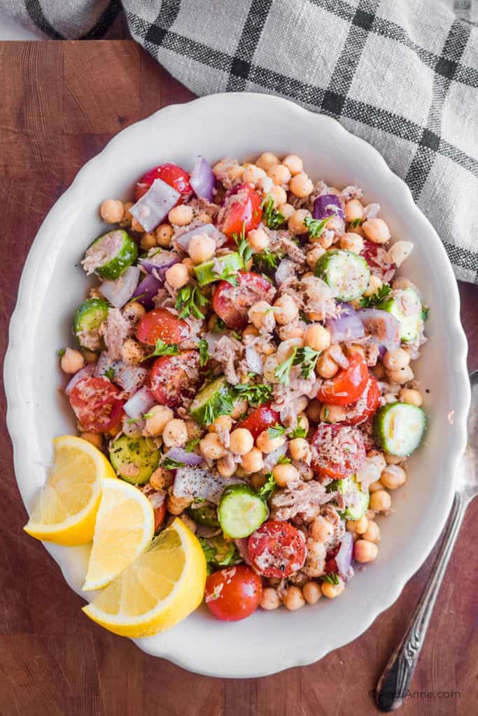 chickpea lemon tuna salad in a white serving bowl with lemon wedges on the side.