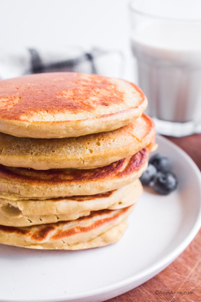 stack of quinoa flour pancakes on white plate. Glass of milk in background.