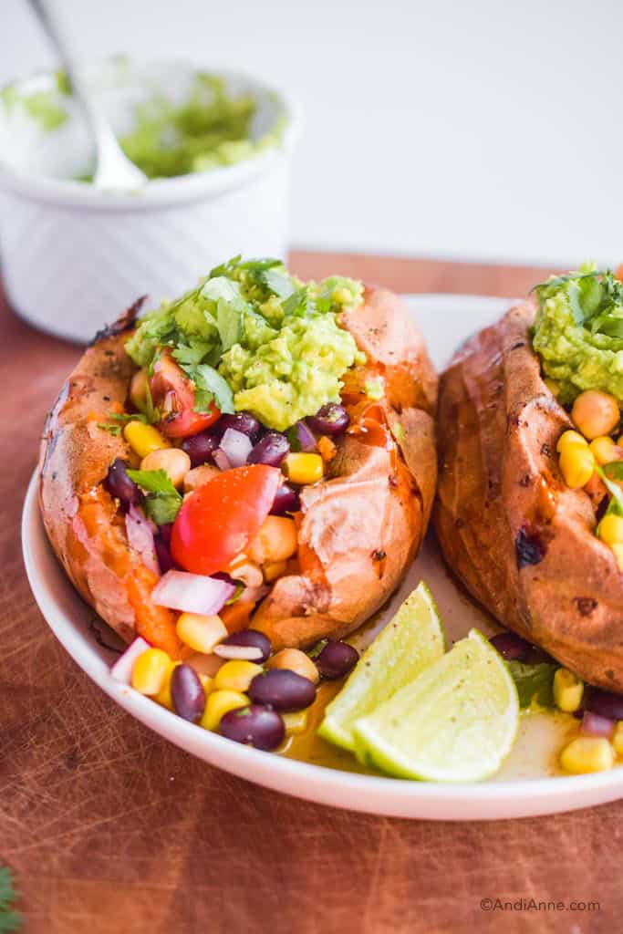 Taco stuffed sweet potatoes on a white plate with two limes. White bowl in the background.