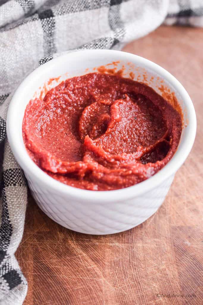 homemade barbecue sauce in a white bowl with kitchen towel behind it.