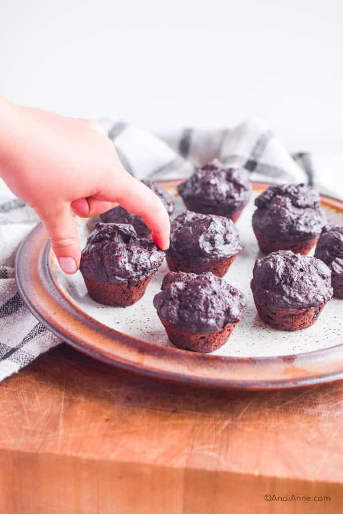 kids hands picking up a mini muffin from a brown plate
