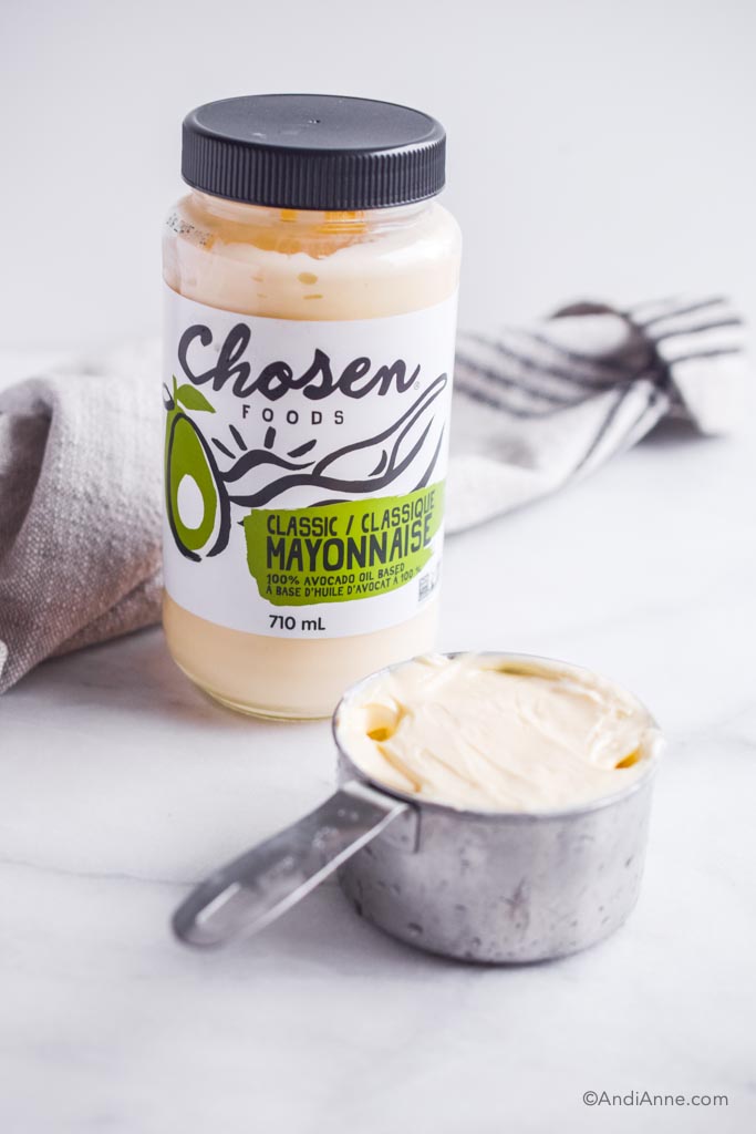 jar of chosen foods avocado mayonnaise  with measuring cup in front and kitchen towel in back