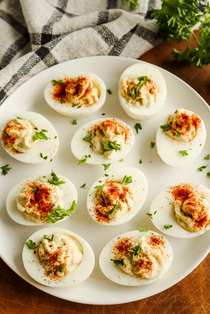 Deviled eggs on a white plate sprinkled with paprika and parsley.