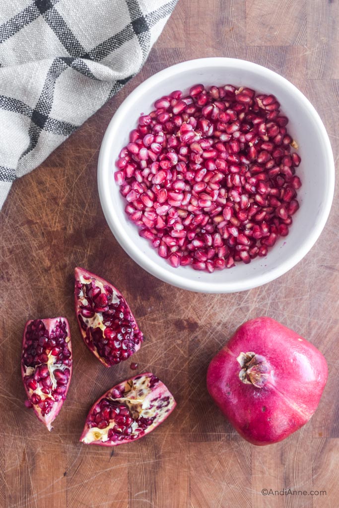 bowl of pomegranate seeds, sliced pomegranate and whole pomegranate on a wood cutting board