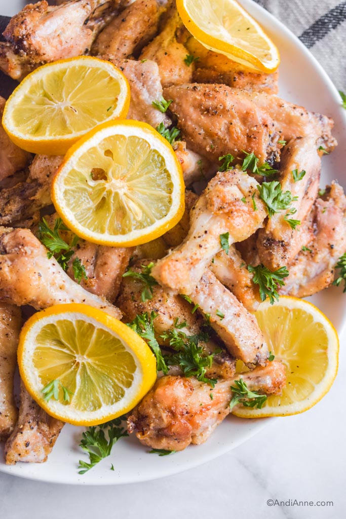 close up of baked sliced lemons and chicken wings on white plate. Bits of parsley are sprinkled on top.