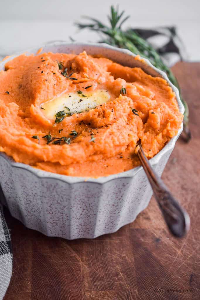 mashed sweet potatoes in a white bowl with melted butter and fresh thyme sprinkled on top.