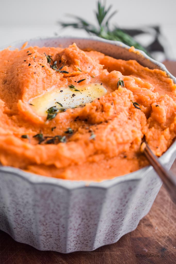 Close up of mashed sweet potatoes in white bowl with melted butter on top.