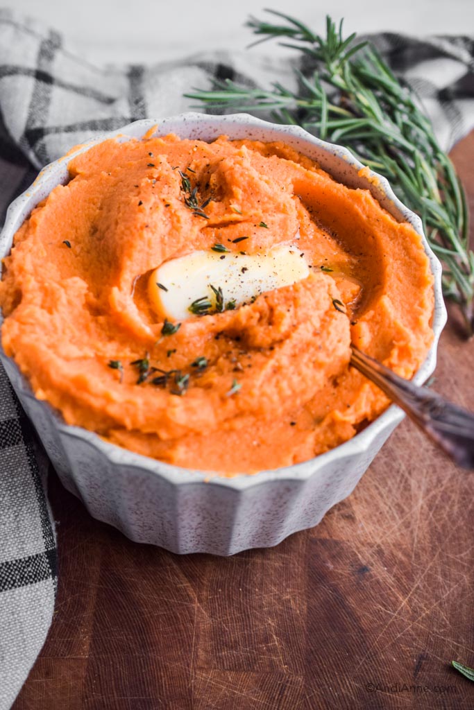 mashed sweet potatoes in a white bowl with melted butter and fresh thyme on top - healthy holiday recipes