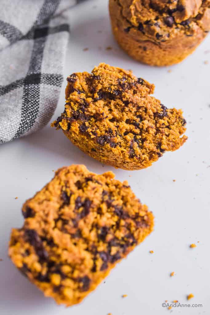 one pumpkin muffin cut in half. Full muffin and kitchen towel beside it.