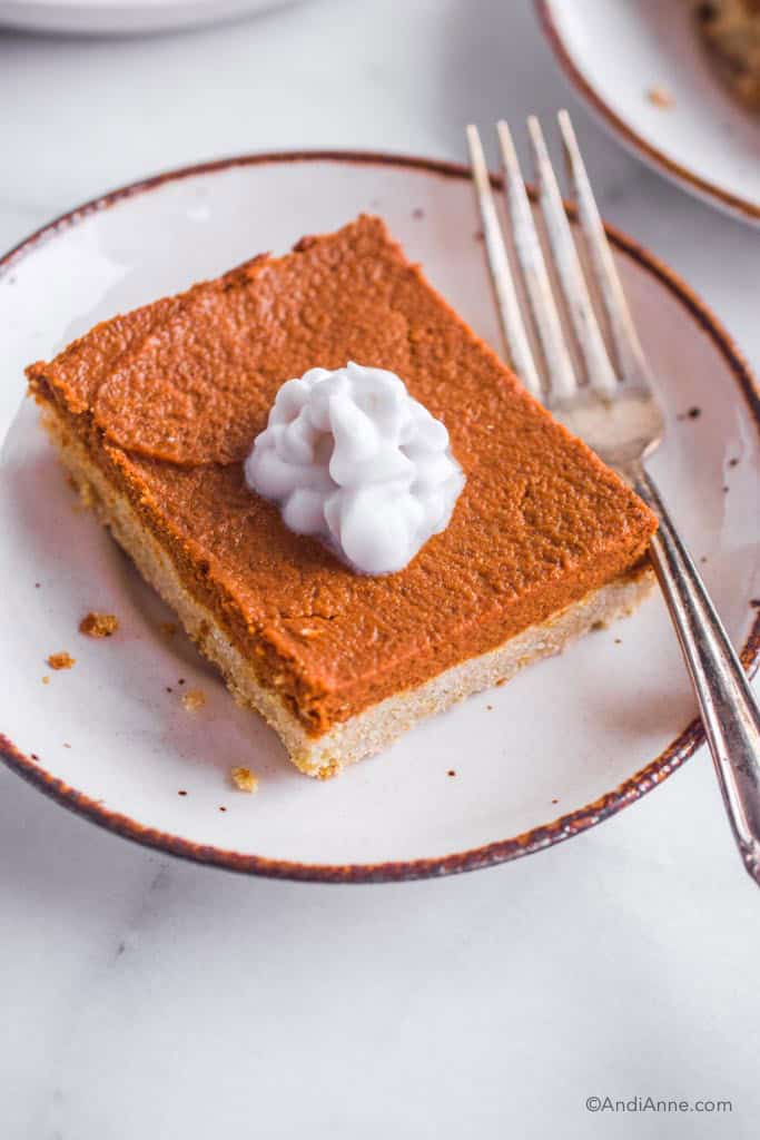 close up of slice of pumpkin pie bar with coconut cream on a white plate with a fork