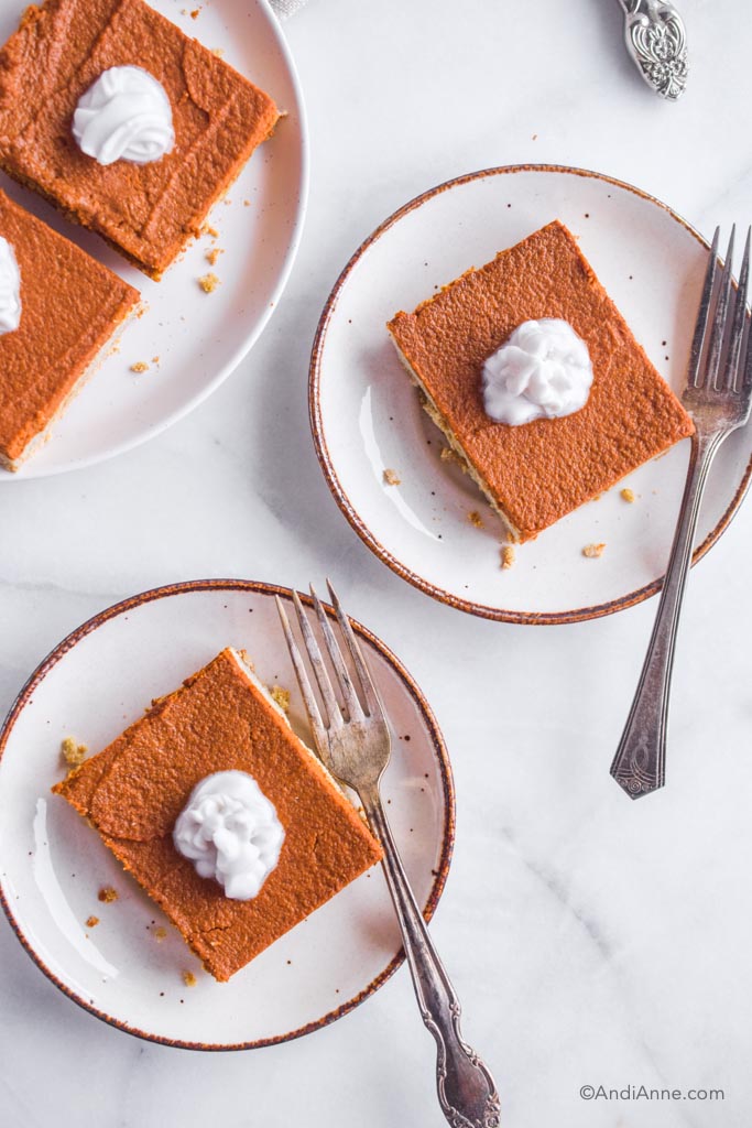 pumpkin pie bars on white plates with fork on the side. Dollop of whipped coconut cream in the center.
