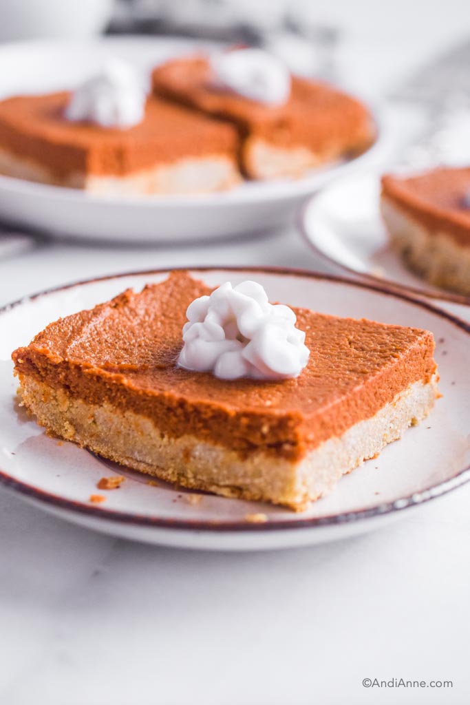 Side angle of pumpkin pie bars on white plate with dollop of whipped coconut cream on top