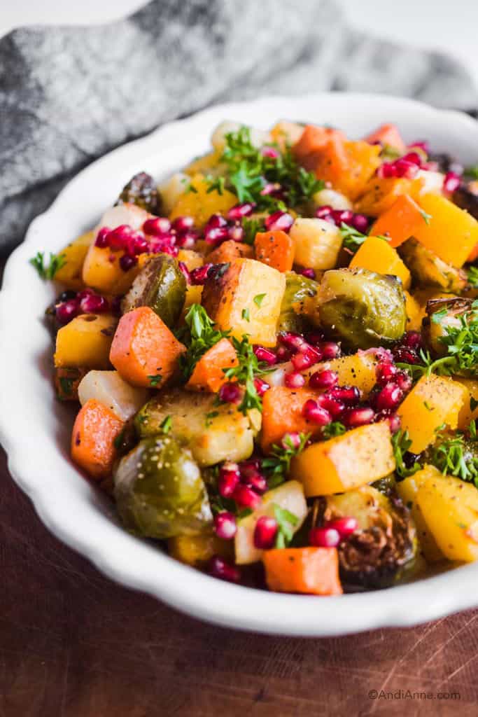 close up of white dish with roasted root vegetables, pomegranate seeds and parsley