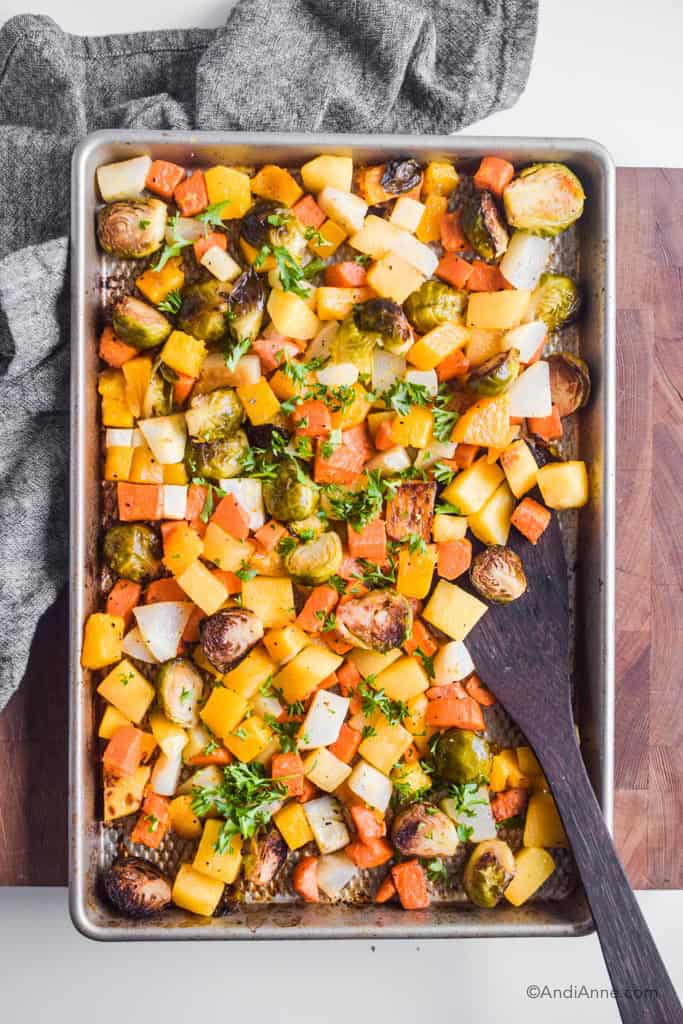 Chopped roasted root vegetables on a baking sheet with wooden spatula on side.