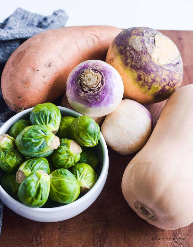 sweet potato, brussels sprouts, butternut squash, turnip and rutabaga on a wood cutting board.