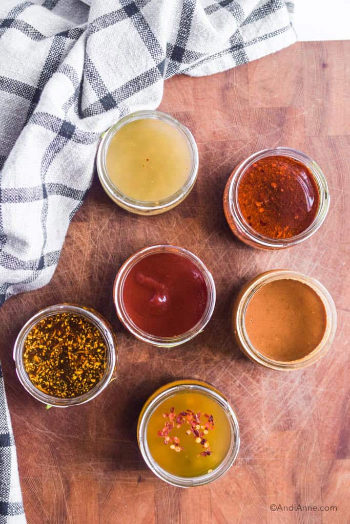 six jars of different stir fry sauces on wood butcher blog with kitchen towel beside them