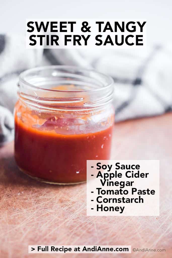 sweet and tangy stir fry sauce in a glass jar on a wood board with kitchen towel behind it.