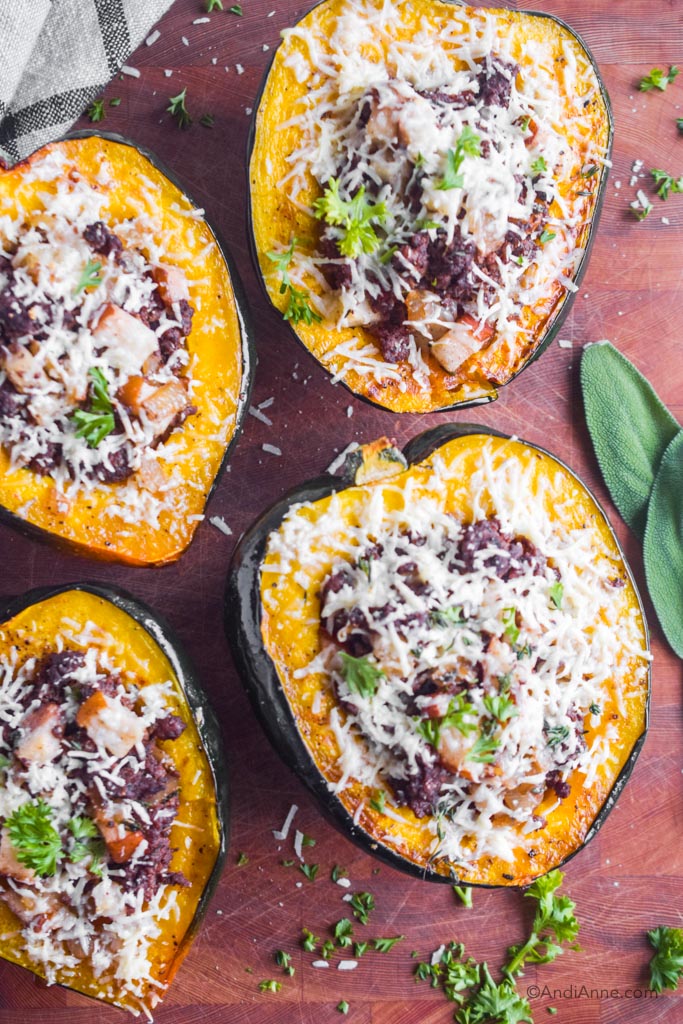 stuffed acorn squash with ground beef, pears and grated parmesan on a wood cutting board.