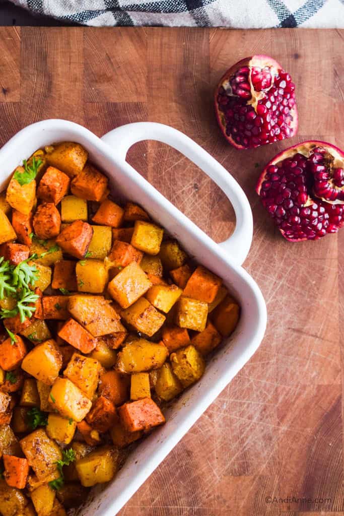looking down on white tray of squash and sweet potato cubes in cinnamon. Open pomegranate is beside.