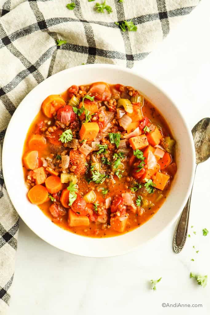sweet potato soup in a white bowl with a metal spoon and kitchen towel surrounding the bowl