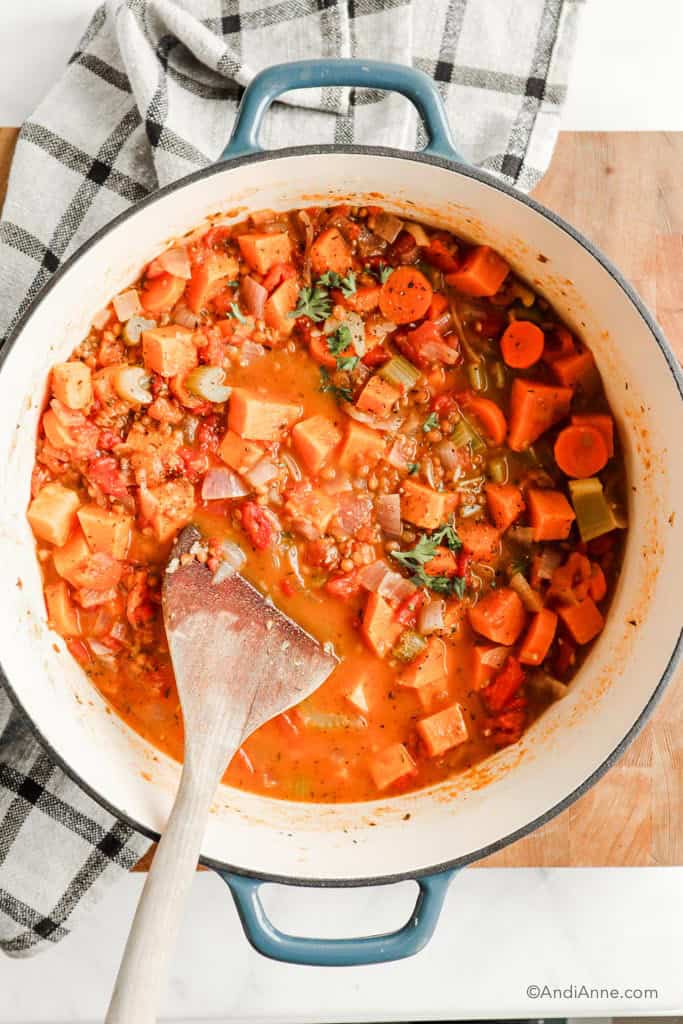 sweet potato soup with carrots and lentils in a large cast iron enameled pot with blue edges. Wooden spoon is inside the pot.
