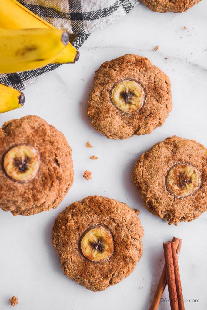 Banana bread cookies on white marble with bananas and cinnamon sticks surrounding them