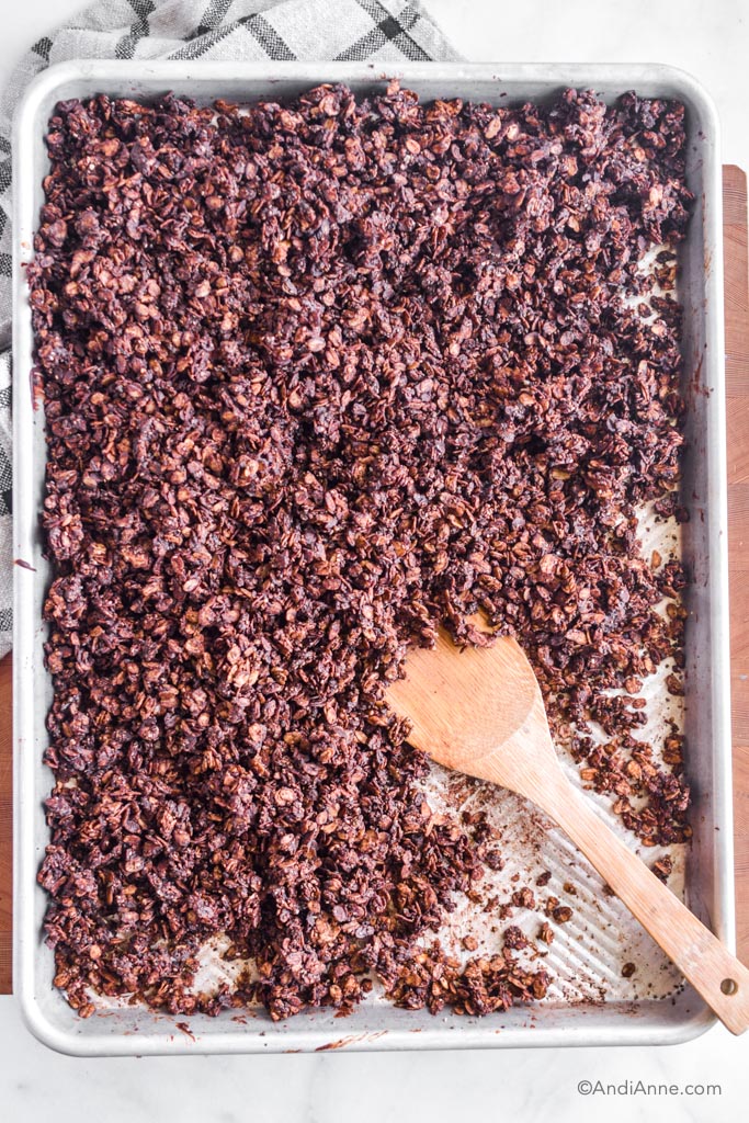 chocolate granola on a baking sheet with a wooden spoon