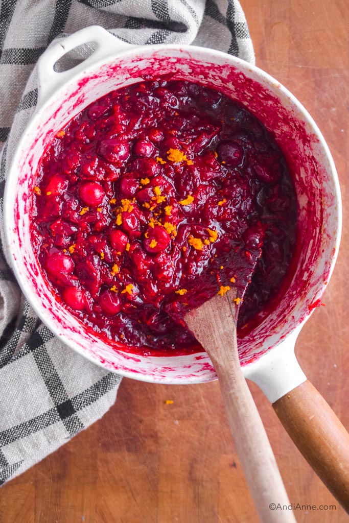 cooked cranberry sauce in a white pot with wooden spoon.