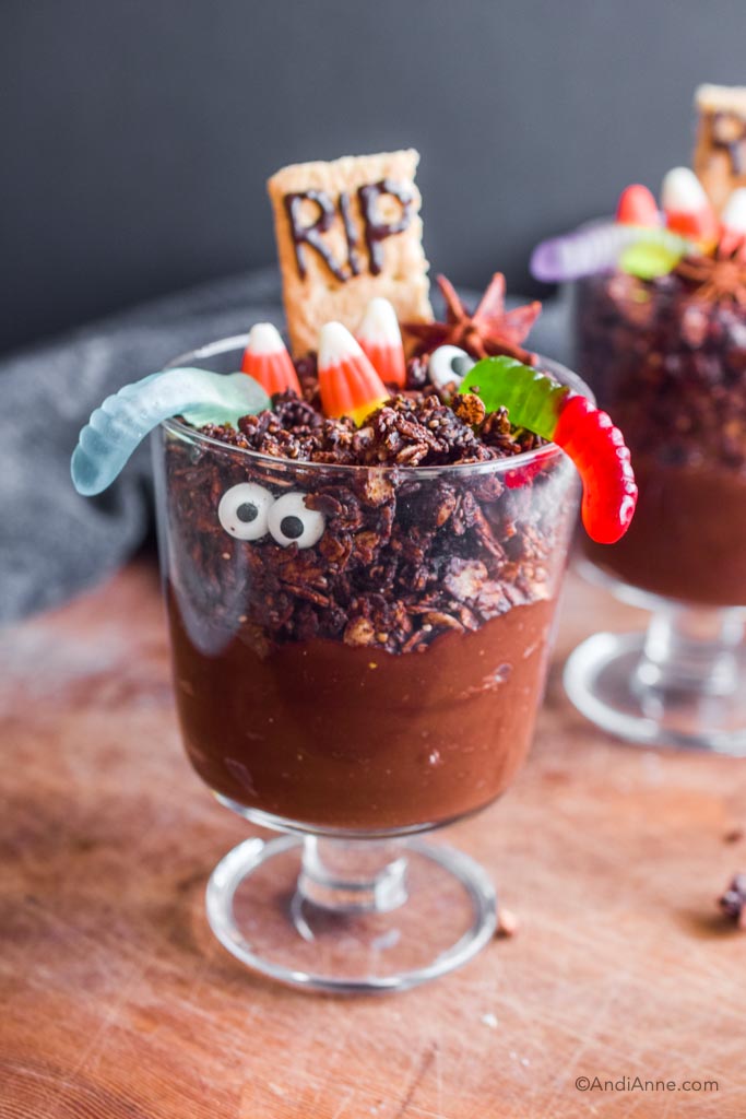 Chocolate graveyard dirt cups kids recipe in a glass container topped with different halloween candies.