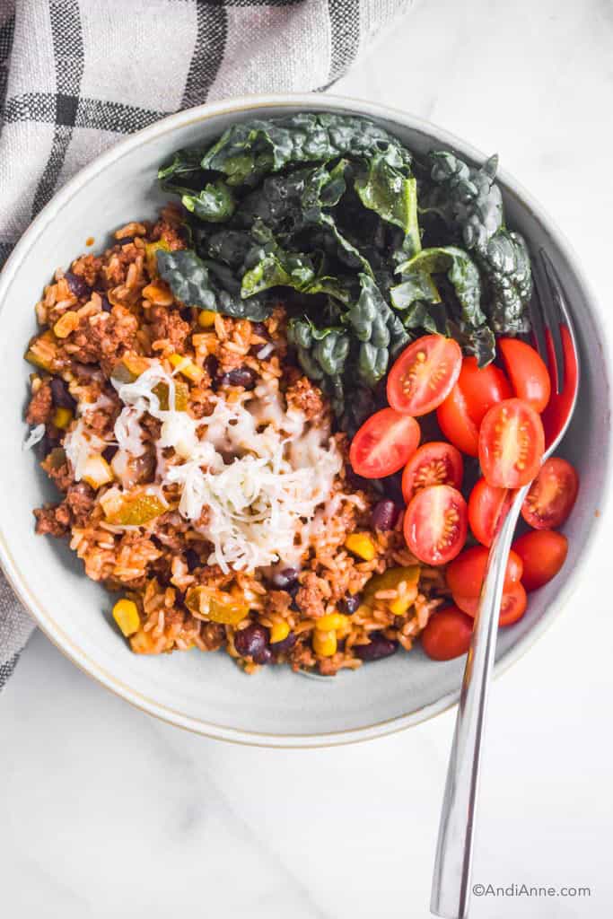 Instant Pot Beef Burrito Bowls with burrito bowl rice, chopped kale, and sliced cherry tomatoes. Topped with mozzarella cheese. In a bowl with a fork on the side.