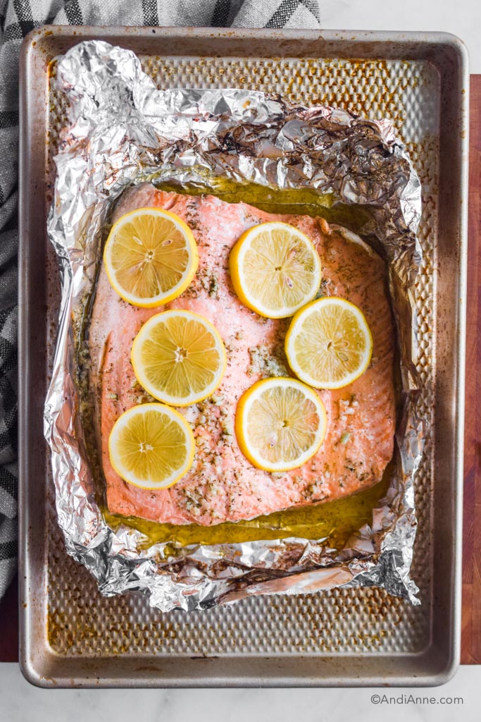 baked steelhead trout in foil with lemon slices on top. All sitting on a baking sheet.