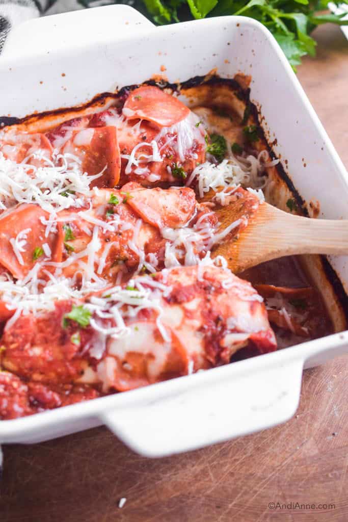 low carb pizza chicken in a white dish with wooden spoon. Extra mozzarella cheese is sprinkled on top.