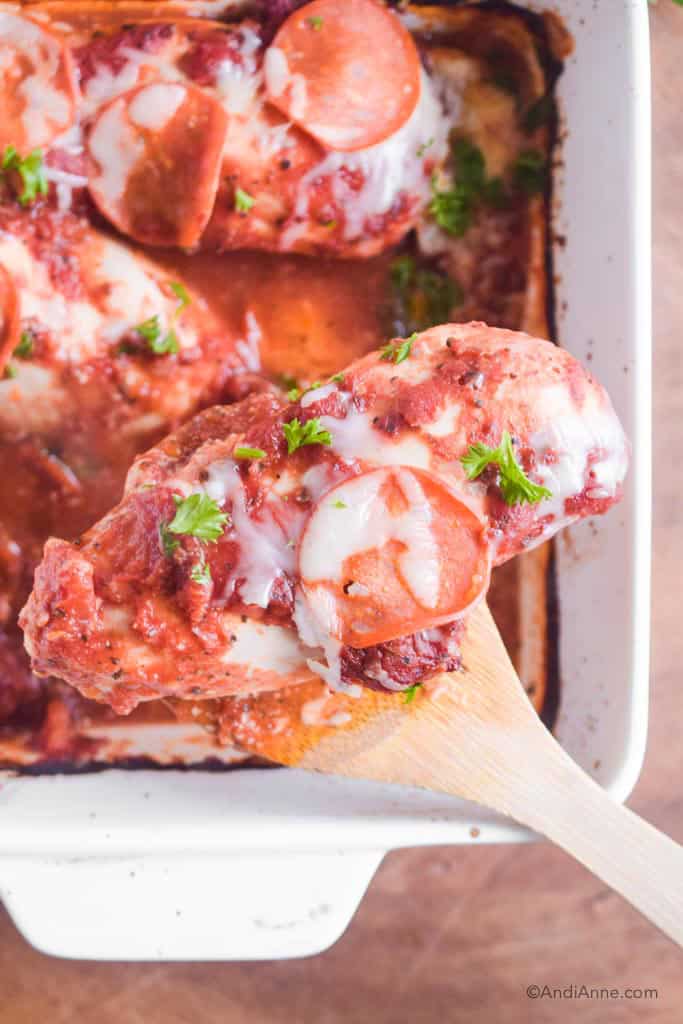 Wooden spoon holding a chicken breast with pizza sauce, pepperoni slice and melted cheese on top.