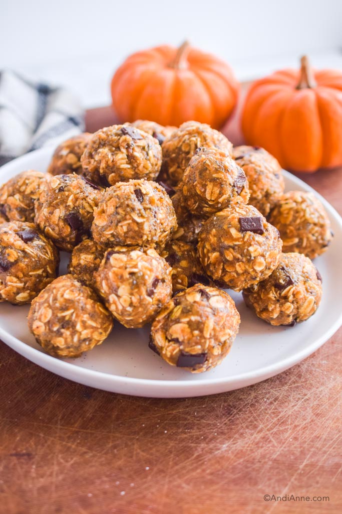 pumpkin oat energy balls stacked on a white plate with mini pumpkins in the background