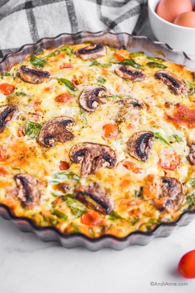 Side angle of crustless quiche with sliced mushrooms, spinach and tomatoes.