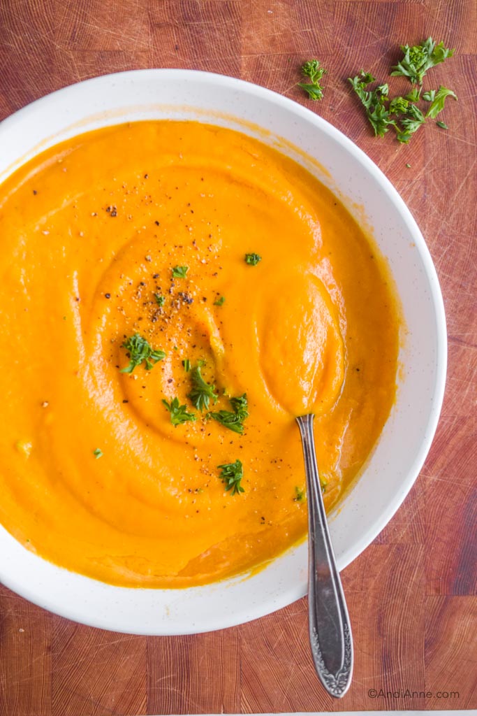 roasted rutabaga carrot soup in a white bowl with a sprinkle of pepper and chopped parsley in the center.