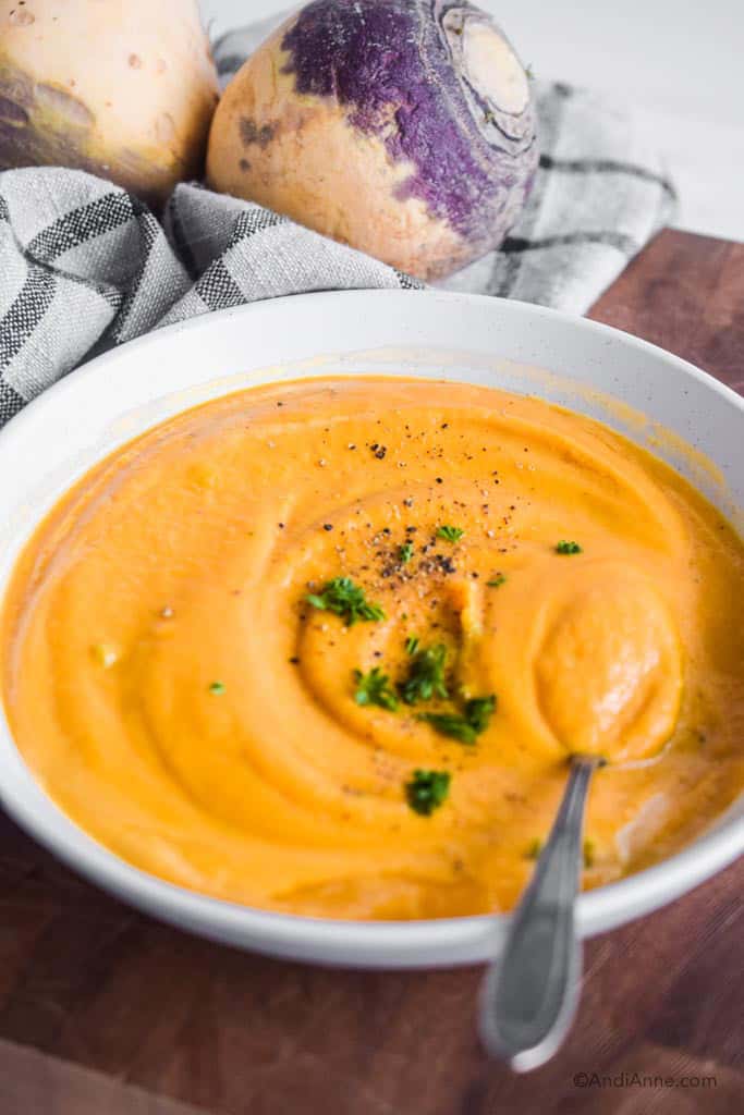 pureed rutabaga soup in a white bowl with two large raw rutabagas in the background