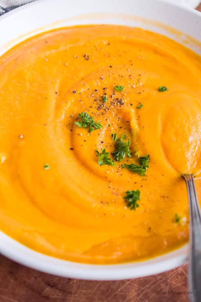Close up of the pureed orange soup with pepper and chopped parsley and a spoon