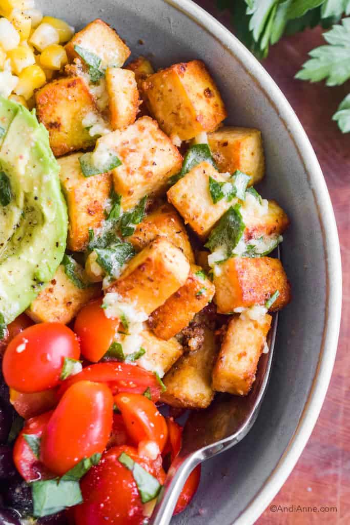 close up of crispy tofu beside cherry tomatoes in light blue bowl.