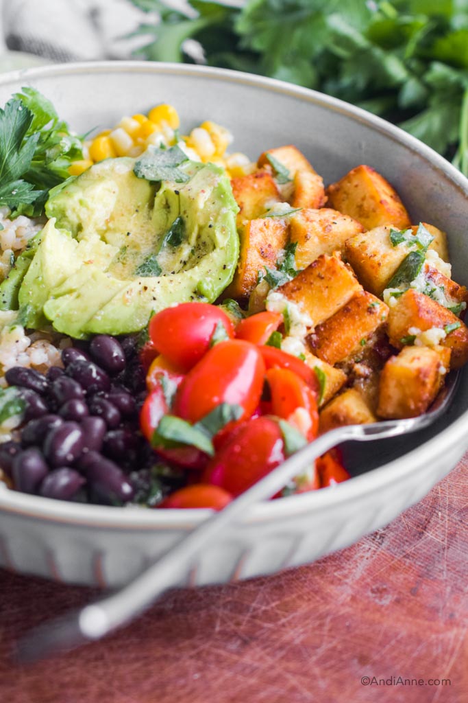 close up of crispy tofu, cherry tomatoes, avocado and black beans in a blue bowl.