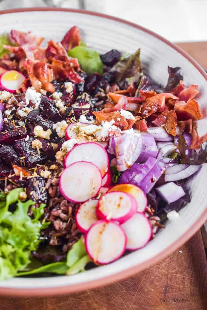 close up of radishes, onion, bacon, beets and goat cheese inside salad.