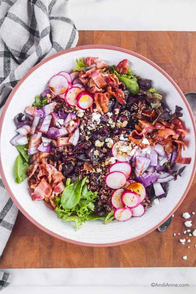 roasted beet bacon feta salad inside white bowl with kitchen towel and spoon beside it.
