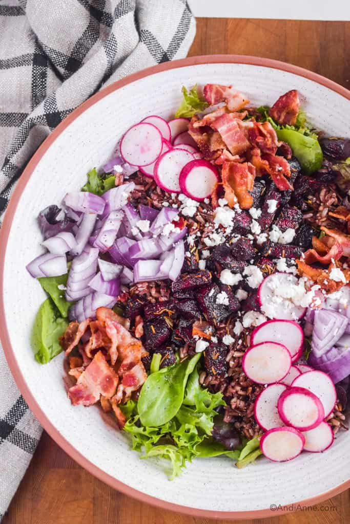 beet bacon feta salad in a white bowl with kitchen towel beside it.