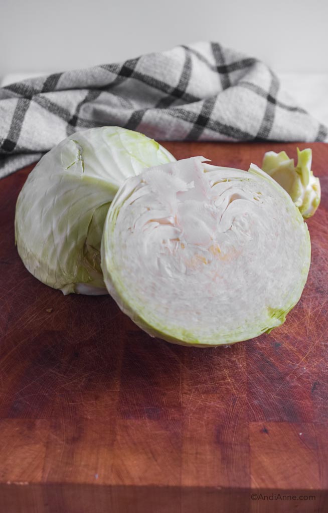 1 small head of cabbage sliced in half on a butcher block.