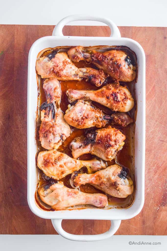 looking down at a white casserole dish with baked chicken wings. sitting on a butcher block cutting board.